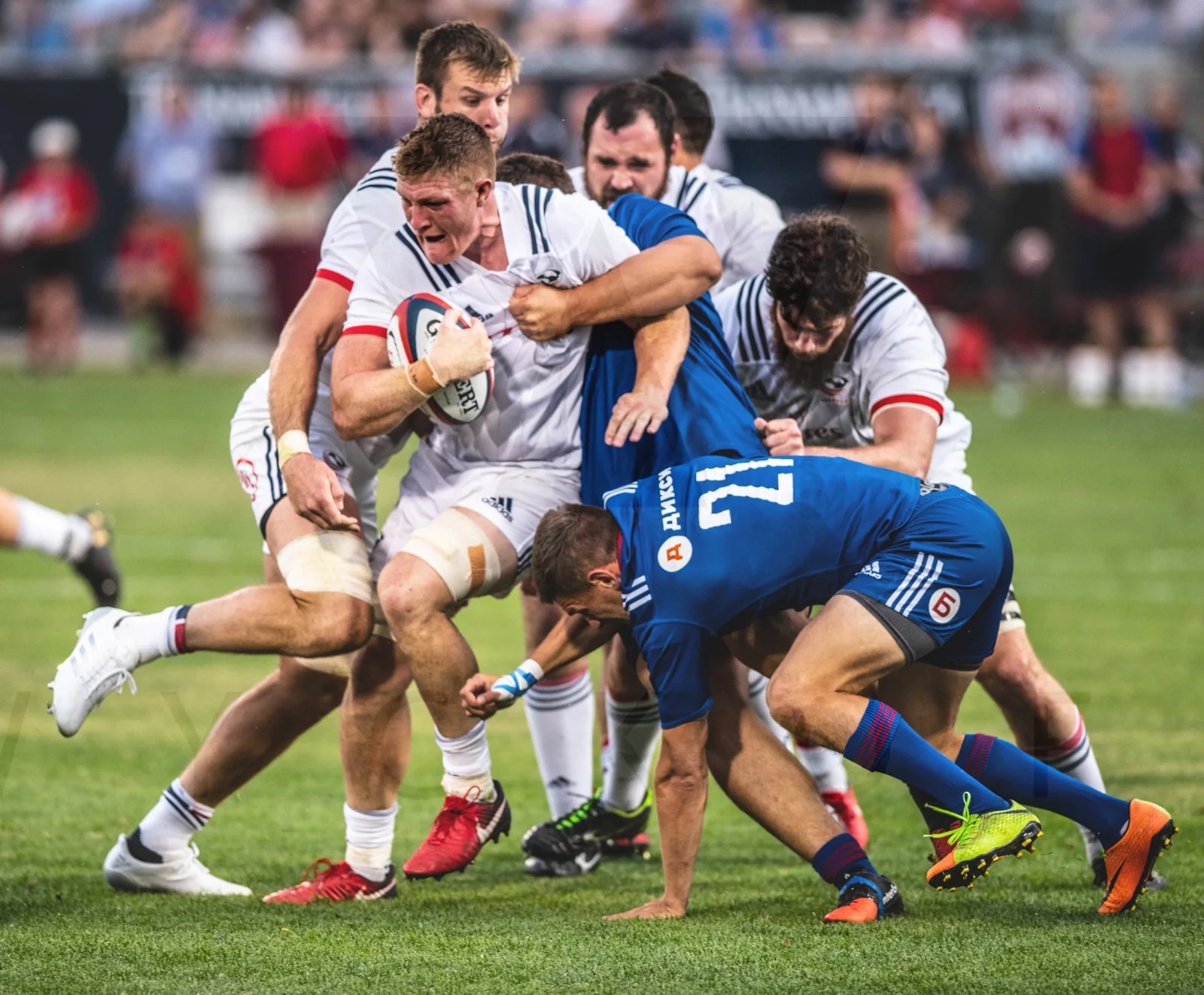 A rugby player carrying the ball drives forward through several tacklers